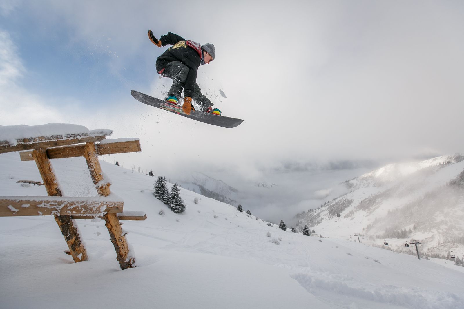 A snowboarder catching air on a snowy resort slope with chairlifts behind